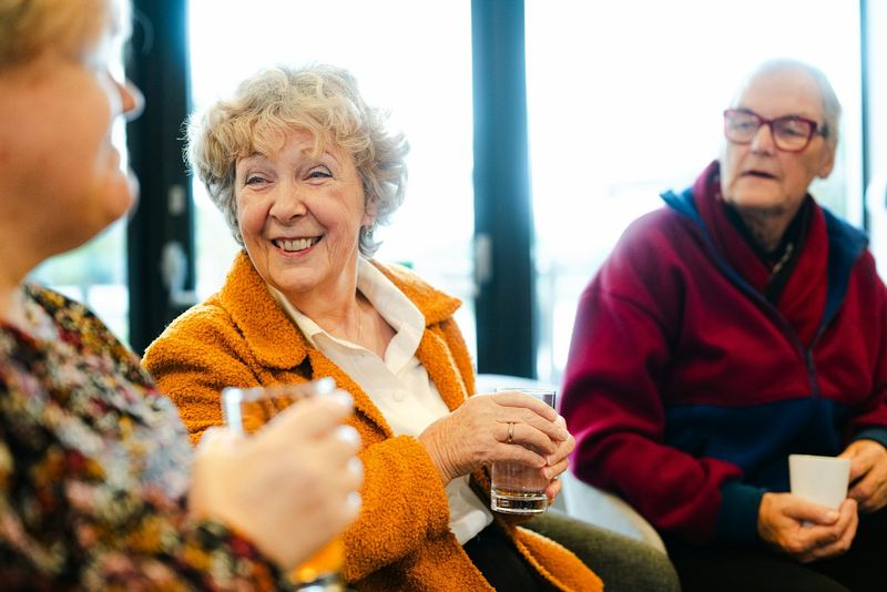 A smiling woman in her seventies chatting with friends over coffee
