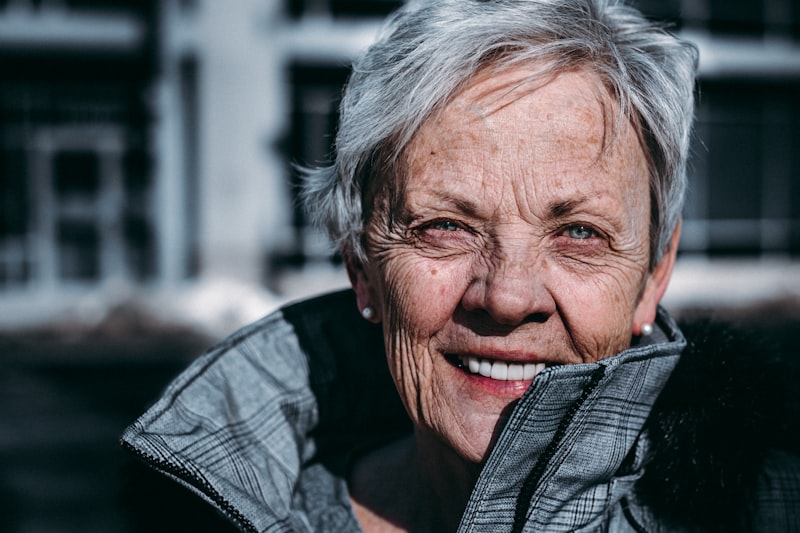 A smiling woman with silver hair outdoors in a warm jacket